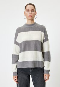 Grijze en crème gestreepte trui met een ribbeltextuur, hoge hals en een losse pasvorm. Heeft lange mouwen en een rechte zoom.