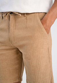 Beige linnebyxor med fiskbensmönster, utrustade med sidofickor och dragsko i midjan. Texturerad tyg med en avkopplad passform.