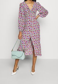 Kwiatowa sukienka midi z dekoltem w serek, długimi bufkowymi rękawami i przednim rozcięciem. Wzory w odcieniach różu, fioletu i zieleni. Do kompletu jasnoniebieska torebka.