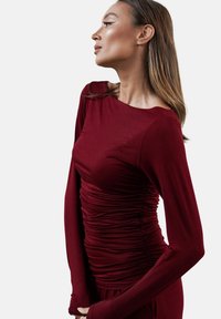 Burgundowa bluzka z długim rękawem z elastycznego materiału, z bocznym marszczeniem i szerokim dekoltem, zapewniająca dopasowany krój i gładką fakturę.