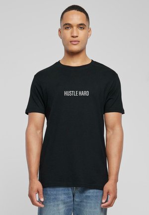 Black cotton t-shirt featuring short sleeves and a round neckline. The front displays the text "HUSTLE HARD" in white, centered.