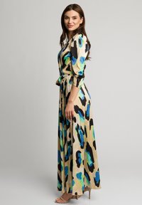 Długa, zwiewna sukienka o beżowym tle, z wyrazistym niebiesko-czarnym wzorem w panterkę. Miękka tkanina, fason kopertowy i pas z klamrą.