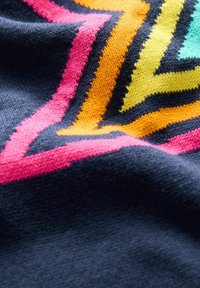 Tessuto a maglia caratterizzato da un motivo geometrico a zigzag in rosa, arancione, giallo e verde acqua su uno sfondo blu scuro. Texture morbida.