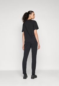 Zwarte katoenen t-shirt met korte mouwen, gecombineerd met zwarte slim-fit broek. De outfit heeft een gladde textuur en een minimalistisch ontwerp.