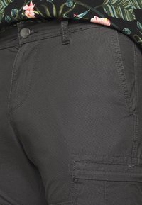 Pantalones cargo de color gris oscuro con una tela texturizada, que cuentan con bolsillos laterales y un cierre de botón. Llevados con una camisa de estampado floral.