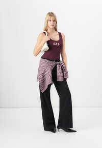Burgundy tank top with "GAP" logo, black wide-leg jeans, checkered shirt tied at waist, and white handbag; model wearing black pointed heels.