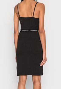Svart figursydd klänning med tunna remmar, tillverkad av mjukt material. Har en Calvin Klein Jeans-logoband i midjan. Slät, minimalistisk design.