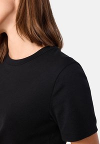 T-shirt nera a maniche corte con scollatura rotonda, realizzata in morbido cotone, che presenta una superficie liscia e cuciture pulite.