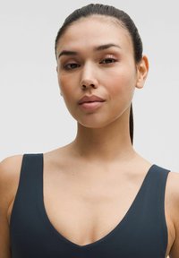 Top de culoare albastru închis, fără mâneci, cu un decolteu adânc în formă de V. Textură de țesătură netedă, stil minimalist, evidențiind gâtul și umerii.