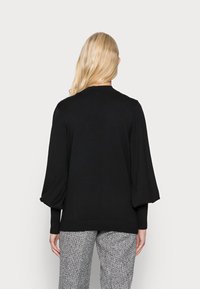 Czarny sweter z dzianiny z balonowymi rękawami i prążkowanym dołem, noszony na spodniach w wzór houndstooth. Tekstura wydaje się miękka i lekka.