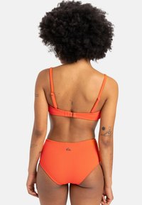 Geribbeld oranje bikini met verstelbare bandjes. Hoge taille broekje. Inclusief een klein logo detail aan de linkerkant. Glad textuur.