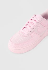 Ροζ αθλητικά παπούτσια Nike με λεία, υφή επιφάνεια που διαθέτει σχέδια καρδιών. Σχεδιασμός με κορδόνια σε ροζ χρώμα που ταιριάζει και λαστιχένια σόλα.