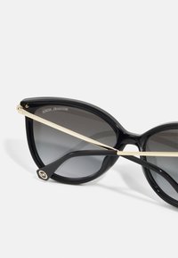 Black plastic sunglasses with oversized, cat-eye frames. Gradient dark lenses, gold metal accents, and logo on temple. Smooth texture.