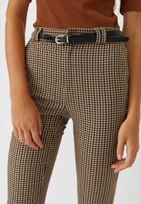 Pantalon à carreaux marron et noir, coupe slim, avec une ceinture noire à motif crocodile et une boucle dorée.