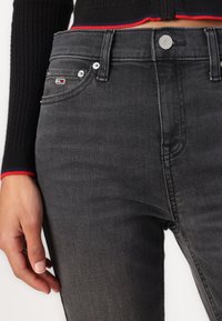 Černé džíny slim fit, s knoflíkovým zapínáním, pěti kapsami a vyšitým logem na kapse. Hladká denimová textura.