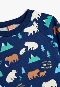 Sudadera marina con una textura suave, con ilustraciones de osos blancos y marrones, pinos verdes y gráficos de montañas. El texto dice: "Las montañas me llaman y debo ir".