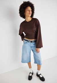 Pulôver cropped castanho brilhante com mangas longas, combinado com calções de denim de perna larga azul claro, meias brancas e sapatos de plataforma pretos.