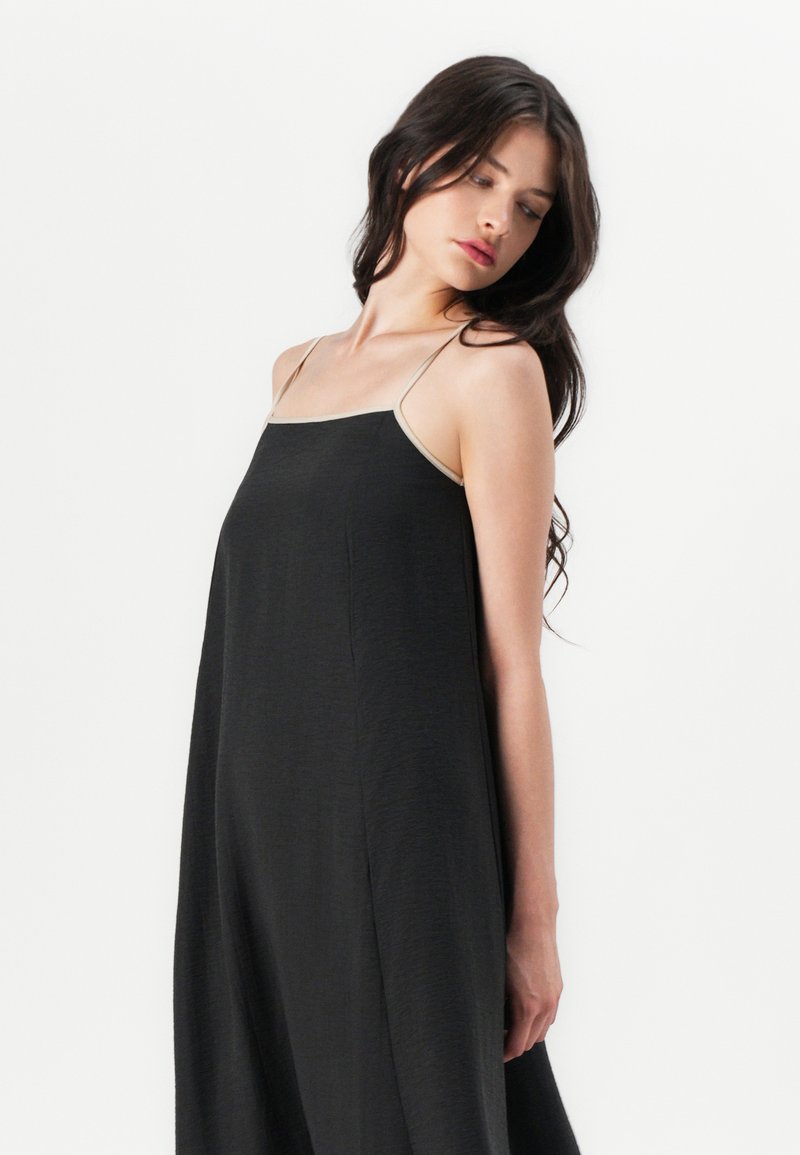 Zwart mouwloos jurkje met dunne banden, met een losse silhouet en zachte textuur. Het jurkje valt tot net onder de kuiten.