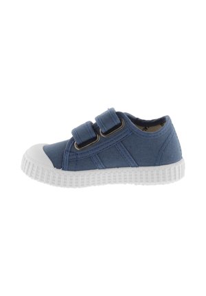 Sneaker en toile bleue avec bout en caoutchouc blanc et semelle texturée, présentant deux bandes auto-agrippantes pour la fermeture et des détails de surpiqûres sur le côté.