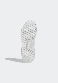 Suela de zapatilla deportiva blanca con un patrón texturizado que presenta indentaciones hexagonales y surcos lineales. La entresuela muestra un detalle de marca en relieve.