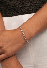Pulsera de cadena de plata con eslabones ovalados interconectados, con un acabado suave y un brillo sutil, llevada en una muñeca sobre un fondo claro.