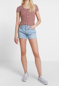 Czerwono-biała bluzka z krótkim rękawem w paski, z okrągłym dekoltem i zapięciem na guziki; połączona z jasnoniebieskimi szortami dżinsowymi i szarymi trampkami.