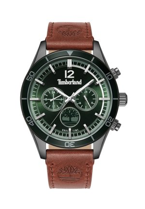 Apaļš rokas pulkstenis ar zaļu ciparnīcu, baltām atzīmēm, dubultā laika displeju un brūnu ādas siksniņu, uz kuras ir iegravēts koka logotips. Metāla korpuss.