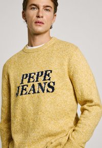 Geltonas megztinis su tekstūros mišiniu, su tamsiai mėlynu "PEPE JEANS" logotipu centre ir apvaliu iškirpimu.