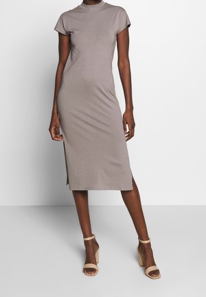 Vestido gris de mezcla de algodón con cuello alto y mangas cortas, con aberturas laterales y silueta ajustada. Combinado con sandalias de tacón beige.