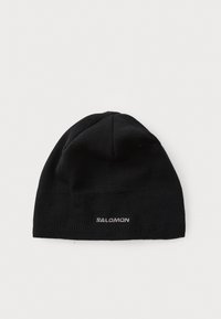 Čierna pletená čiapka z jemného materiálu. Má priliehajúci strih a malé biele logo "SALOMON" na prednom okraji.