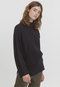 Top lung cu mâneci lungi de culoare purpuriu, cu guler înalt, având o buzunar frontal, textură moale și slits laterale, asortat cu pantaloni maro cu model.