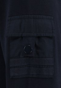 Marineblaues Gewebe mit strukturierter Oberfläche. Verfügt über eine Klappentasche mit Druckverschluss und elastischen Bändern. Insgesamt kompaktes und funktionales Design.