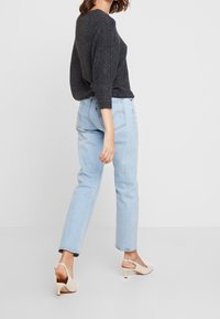 Grå stickad tröja, ljusblå raka jeans och krämfärgade klackskor. Tröjan har en rundad halsringning och lös passform. Jeans har minimal detaljering.