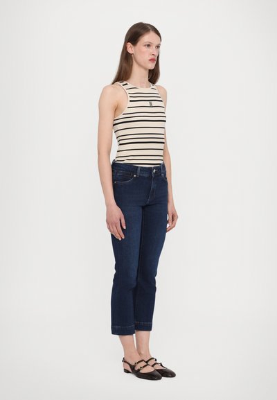 Gestreepte tanktop in crème en marineblauw, gecombineerd met donkerblauwe cropped jeans. Slim-fit ontwerp met een klein logo detail. Zwarte sandalen met bandjes.