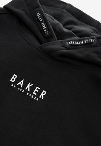 Must kapuutsiga pusa, pehme tekstuuriga, millel on valge trükitud tekst "BAKER BY TED BAKER" ees ja sildid kapuutsi sees.