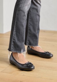 Bailarinas negras con puntera redonda, con una hebilla decorativa. Material suave con un ligero brillo, combinadas con unos vaqueros grises deshilachados.