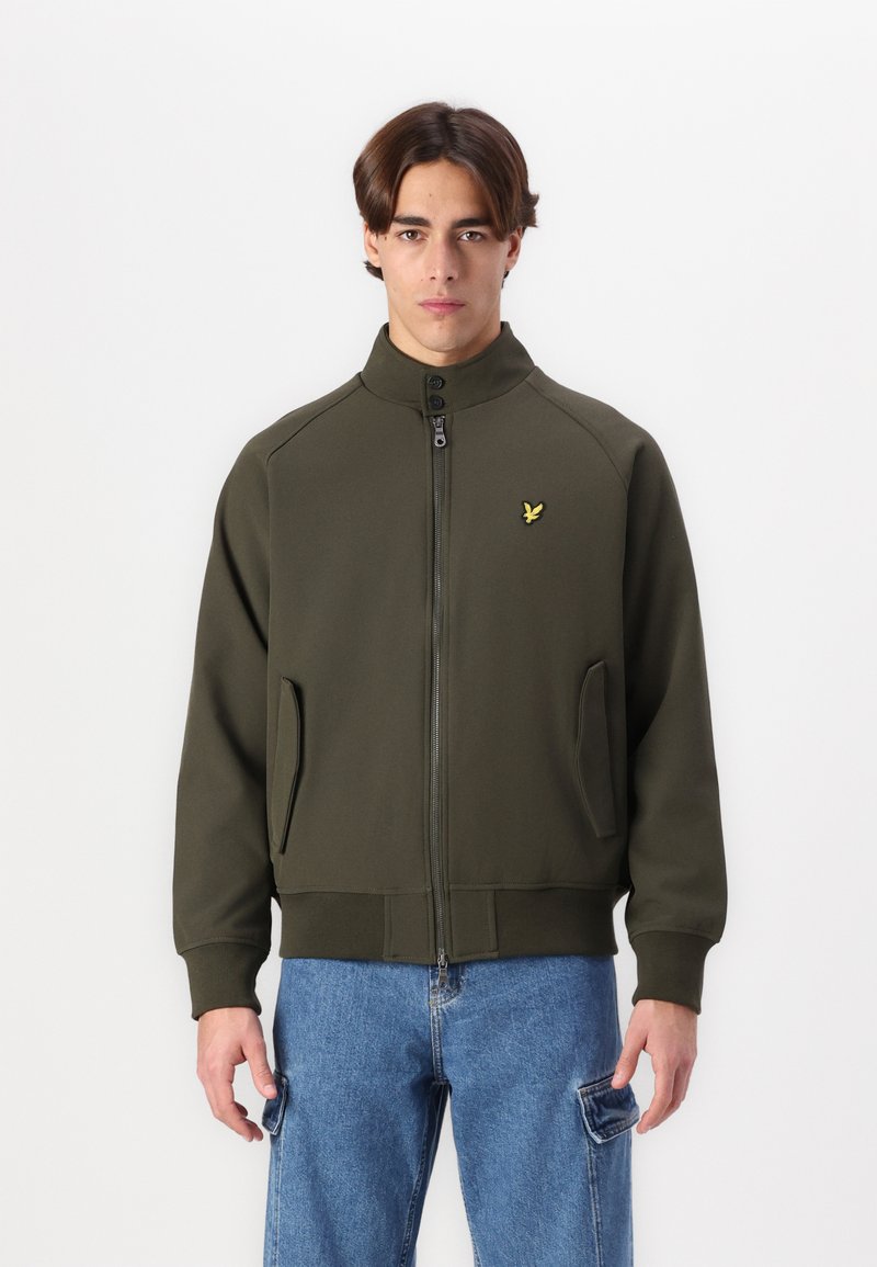 Giacca zippata verde oliva con colletto alto, tasche laterali e un piccolo logo giallo sul lato sinistro del petto. Tessuto liscio e strutturato.