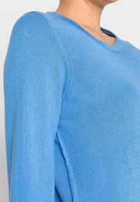 Maglione blu a maglia con collo rotondo, caratterizzato da maniche lunghe, dettagli a coste sul collo e una superficie liscia.
