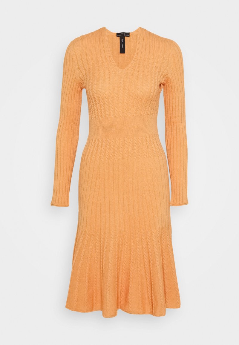 Robe tricotée à manches longues de couleur pêche-orange avec col en V, taille cintrée et jupe évasée, présentée sur un fond uni.
