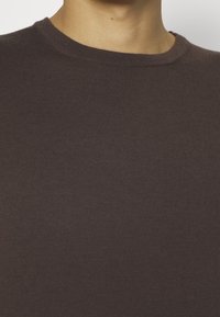 T-shirt marron côtelé avec un col rond, en tissu doux, présentant une surface texturée avec une silhouette ajustée.