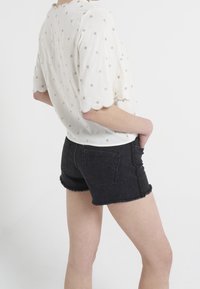 White blouse with gold dot embroidery, scalloped sleeves. Black denim shorts with frayed hems and back pockets.
