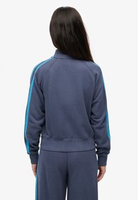 Sudadera azul marino con cuello alto, con franjas laterales turquesas. Textura suave, puños y cintura acanalados. Diseño de corte relajado.