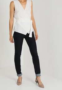 Top bianco con scollo a V profondo e cintura in vita, abbinato a jeans scuri con risvolti e décolleté neutri a punta.