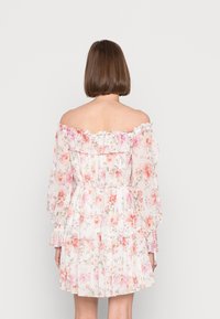 Off-shoulder klänning med blommönster i rosa och vitt, med långa, luftiga ärmar, volangkant och en lager på lager volang längst ner.