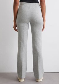 Helle graue, ausgestellte Sweatpants aus einem weichen Baumwollmix, mit hohem Bund und glatter Textur. Sichtbare Nähte entlang der Seiten.