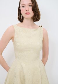 Crème jurk met bloempatroon, een aansluitend lijfje, een uitlopende rok en een unieke gouden accent op de schouder, gemaakt van textured stof.