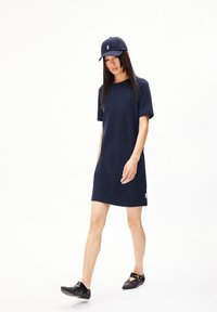 Robe courte à manches courtes bleu marine en tissu lisse, avec une coupe décontractée, assortie d'une casquette et de chaussures noires à enfiler.