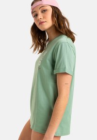 Mintgrøn bomulds T-shirt med korte ærmer, opkrøllede manchetter og trykte blomsterdesigns på forsiden. Glat tekstur, afslappet pasform.