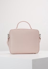 Borsa a mano in pelle di colore rosa pallido, di forma quadrata, con manico superiore e tracolla removibile, su una superficie bianca.