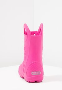 Des Crocs en caoutchouc rose avec une finition lisse, hauteur chevillère, des trous de ventilation circulaires et un logo surélevé au niveau du talon. Semelle texturée pour une meilleure adhérence.